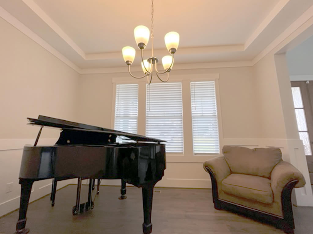 Elegant Faux Wood blinds installed behind a piano and a comfortable chair