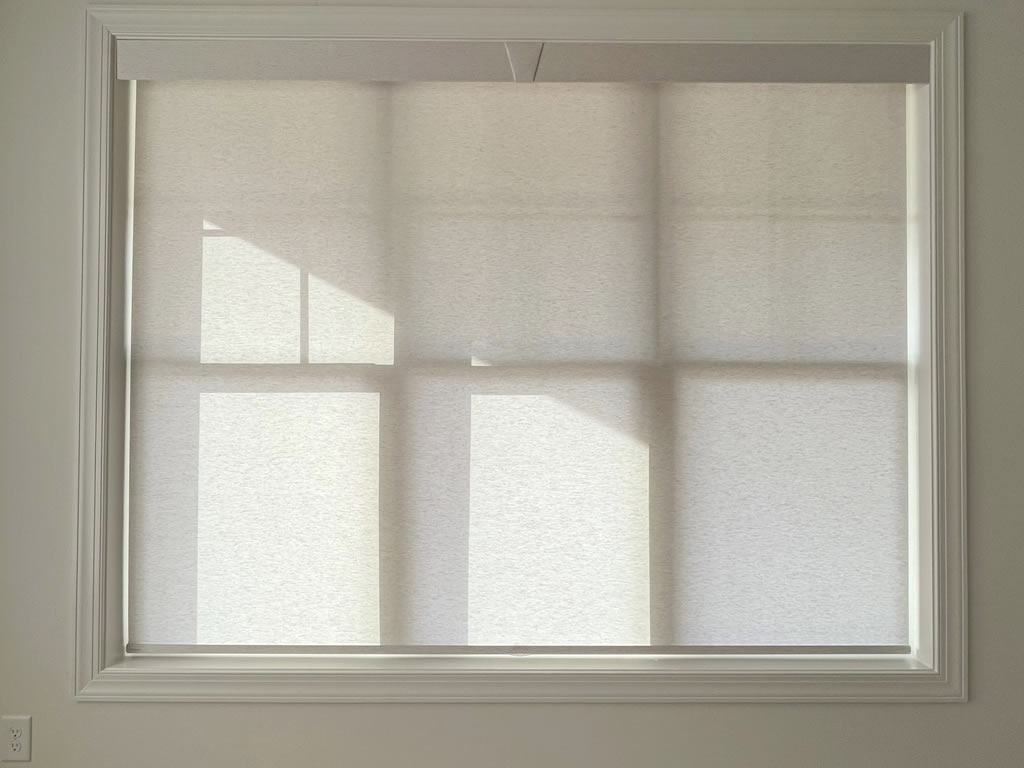 Close-up of a large window with roller shades and decorative top