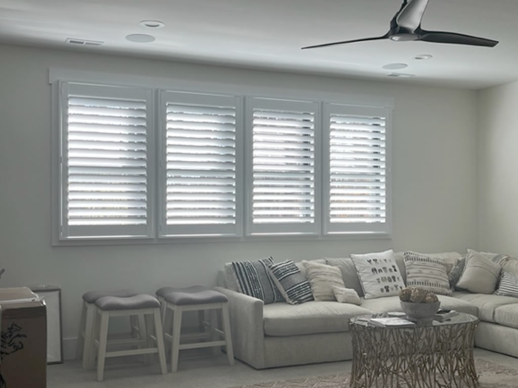 A set of 4 shutters installed over windows in a sitting room with a couch