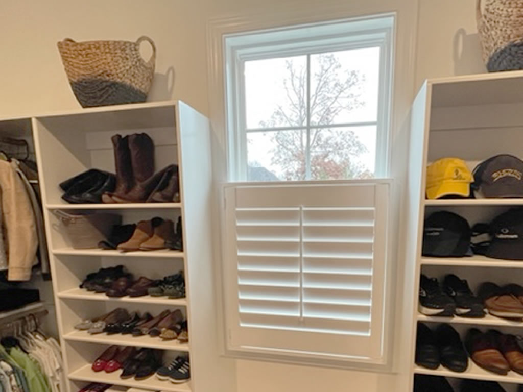 Shutters over a small window in a closet with shelves to either side