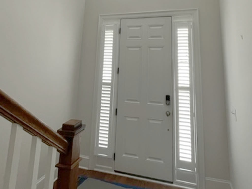 Narrow shutters installed to either side of a front entrance door coving the side windows going up the full height of the door