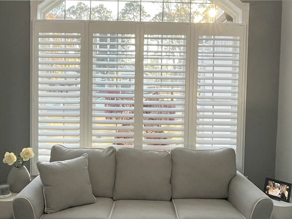 Shutters installed behind a couch in a curved arch window