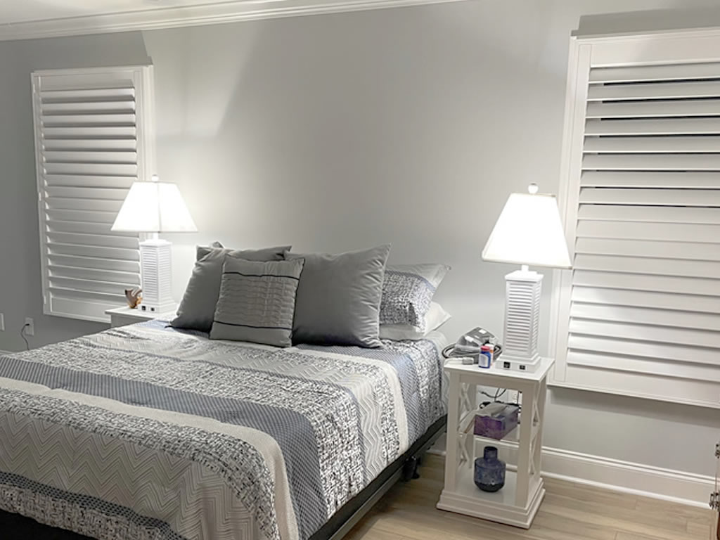 White shutters installed in a bedroom to either side of the bed offering privacy and optimal light control